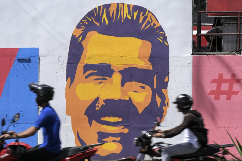 Dos motoristas pasan junto a una pintada con la imagen del actual presidente venezolano y candidato a la reelección, Nicolás Maduro, en el barrio de Catia, en Caracas, el 27 de julio de 2024