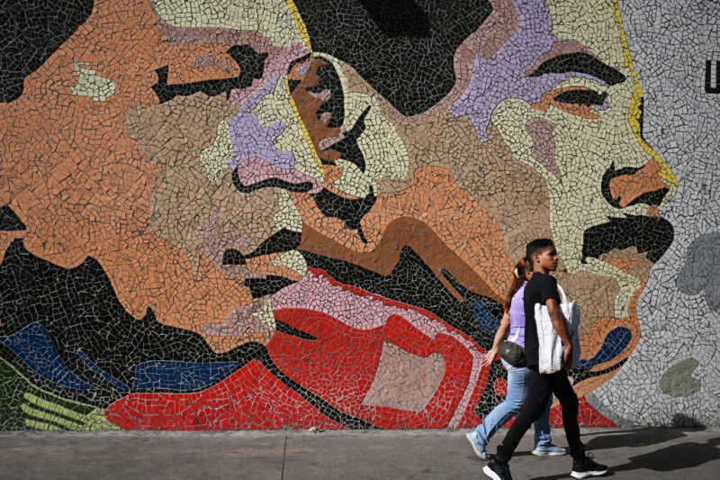 Una pareja camina delante de una pintada con la imagen del fallecido presidente venezolano Hugo Chávez y del actual presidente y candidato presidencial Nicolás Maduro en Caracas el 27 de julio de 2024