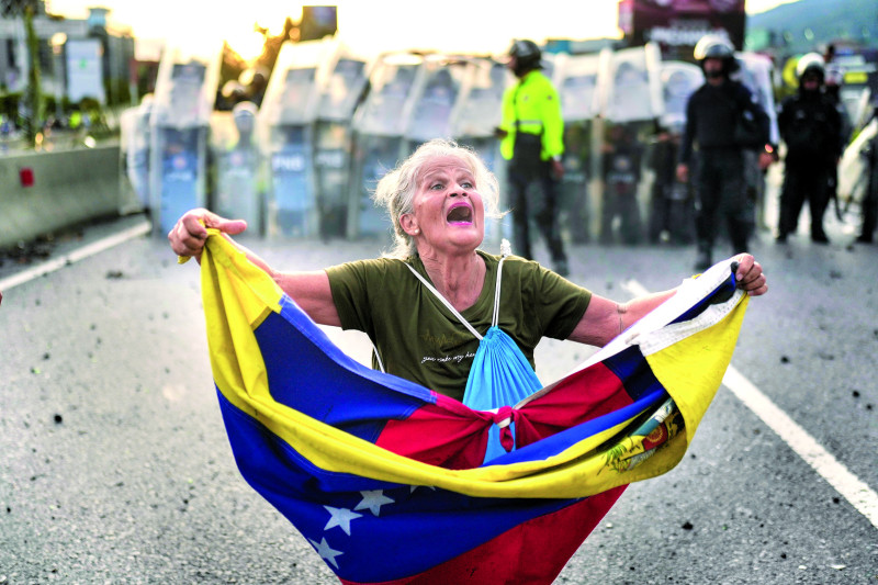 Consuelo Marquez sostiene una bandera venezolana en frente de una barricada de policías el día después de las elecciones, en Caracas.