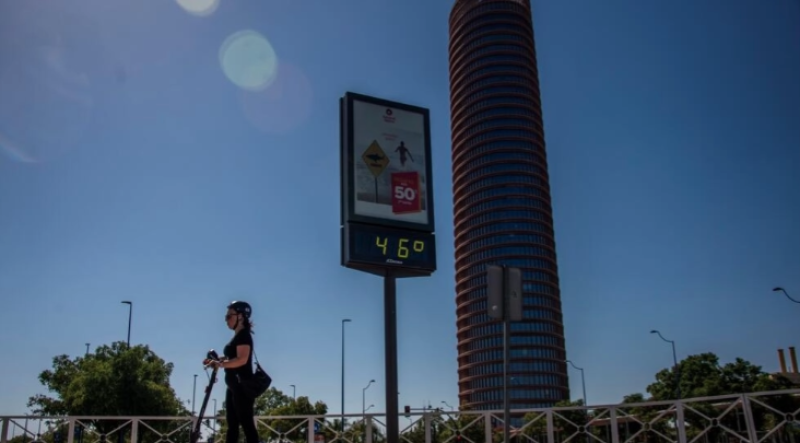 Una mujer pasa en patinete ante un termómetro callejero que marca 46 grados centígrados de temperatura, el 23 de julio de 2024 en la ciudad española de Sevilla.