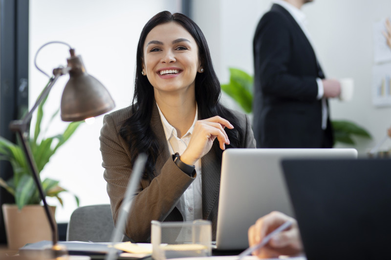 Trabajadora sonriendo con confianza en la oficina. Foto: Freepik.