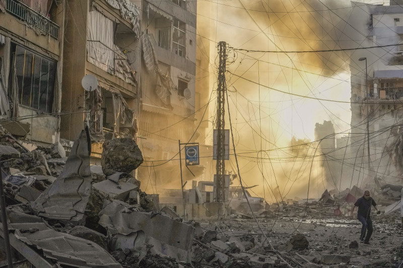 Un hombre corre a ponerse a cubierto mientras de fondo se puede ver el humo provocado por un ataque aéreo israelí en Dahiyeh, Beirut, Líbano, ayer.