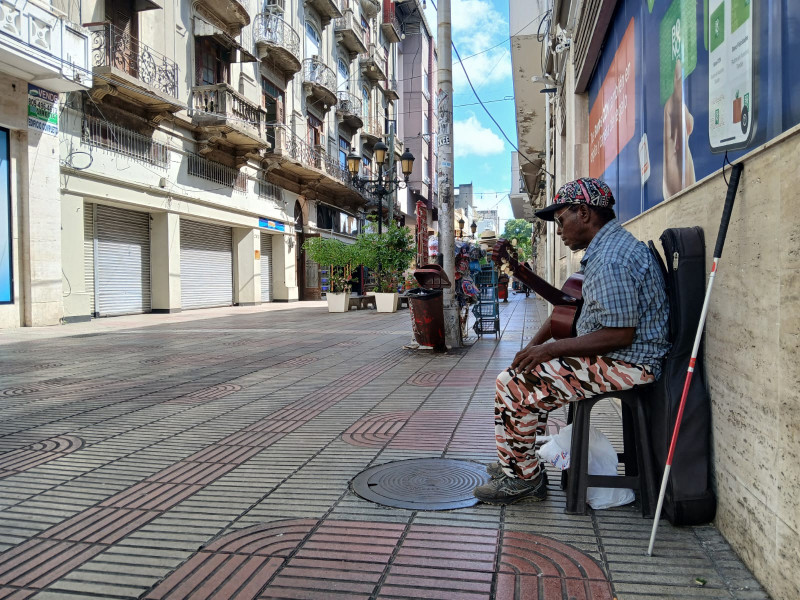 El músico invidente Héctor Pérez, de 66 años, hace una pausa con su guitarra, a la espera de transeúntes por la calle El Conde.