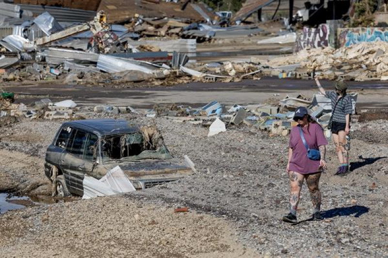 Fotografía del 2 de octubre de 2024 de personas caminando junto a un vehículo afectado luego de las inundaciones provocadas por la tormenta tropical Helene en Asheville, Carolina del Norte (Estados Unidos).