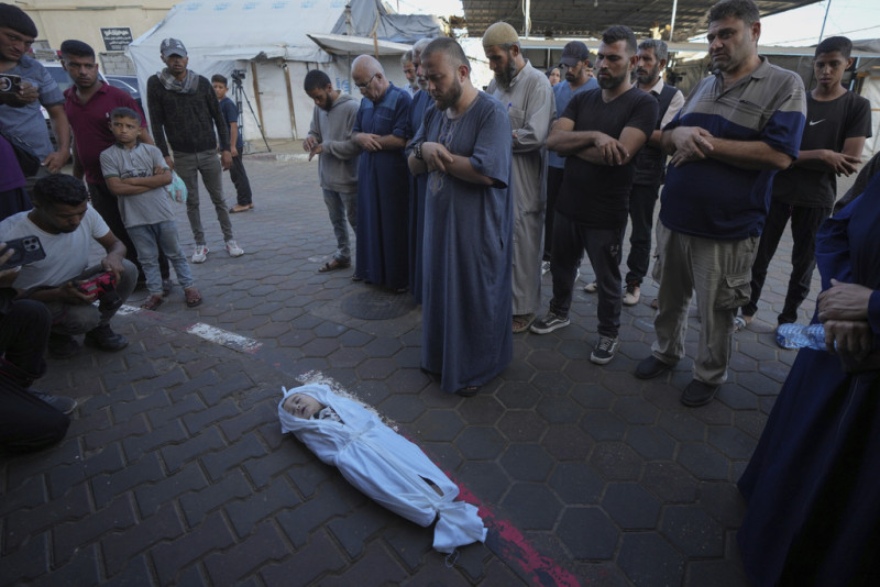 Dolientes rezan sobre el cuerpo de un niño palestino, Hosam Al Khaldi, fallecido en el bombardeo israelí sobre la Franja de Gaza, ante la morgue de un hospital el miércoles 9 de octubre de 2024, en Deir al-Balah