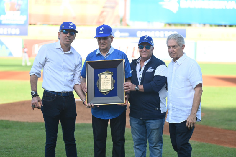 El doctor José Joaquín Puello Herrera, acompañado por su hermano Juan Francisco Puello Herrera, recibe una placa de reconocimiento de manos de Ricardo Ravelo y Miguel Ángel Fernández, presidente y tesorero del Licey, respectivamente.