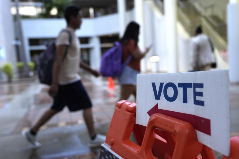 Personas caminan junto a un letrero para votar en el primer día de la votación anticipada de las elecciones generales de Estados Unidos, el 21 de octubre de 2024, en Miami