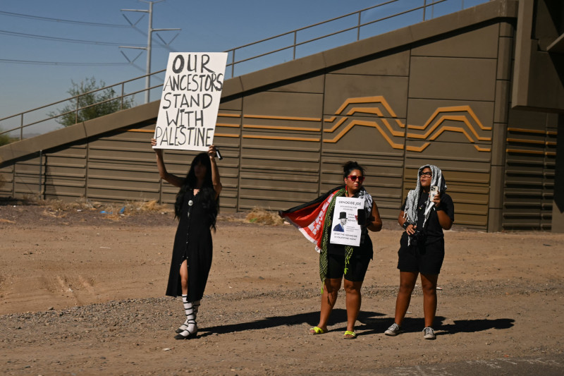 Los manifestantes sostienen carteles mientras la caravana presidencial del presidente estadounidense Joe Biden pasa cerca de Phoenix, Arizona, el 25 de octubre de 2024.