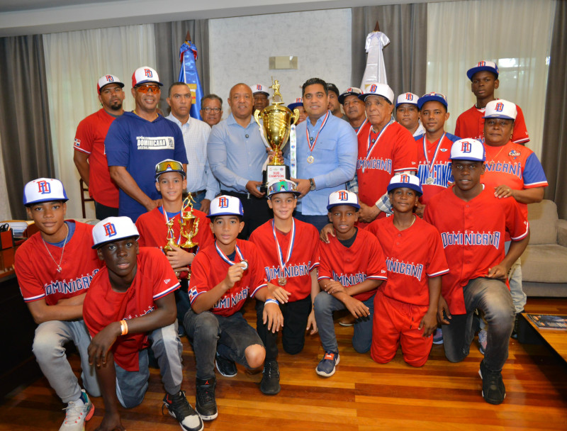 Kelvin Cruz, ministro de Deportes, sostiene el trofeo de campeón con Juan Núñez, presidente de la Federación de Béisbol, quien le visitó ayer junto a la selección de béisbol U-12 Pre Mundial de Béisbol efectuado en Panamá.