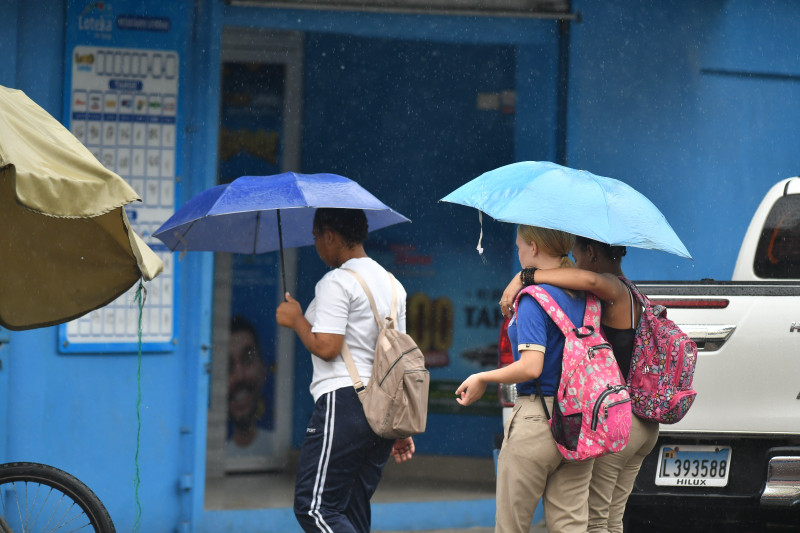 Varios estudiantes se cubren de la lluvia mientras cruzan una calle de la capital.