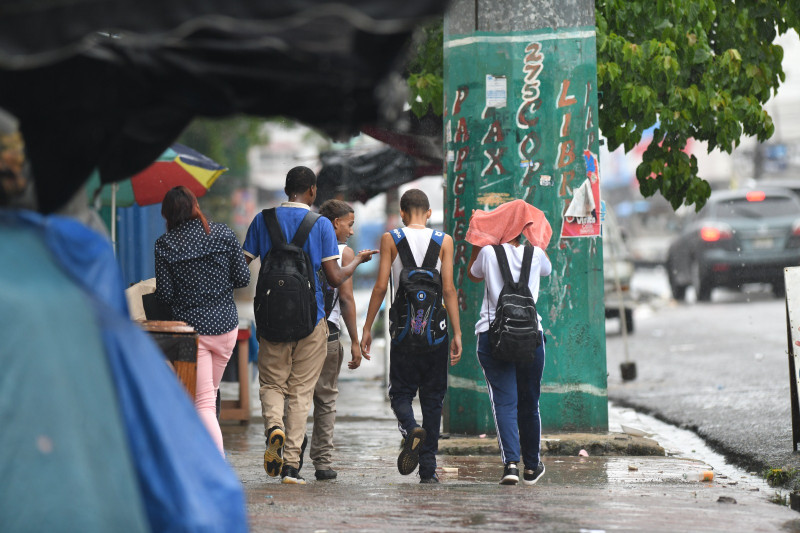 Estudiantes caminan bajo la lluvia en una acera del Distrito Nacional.