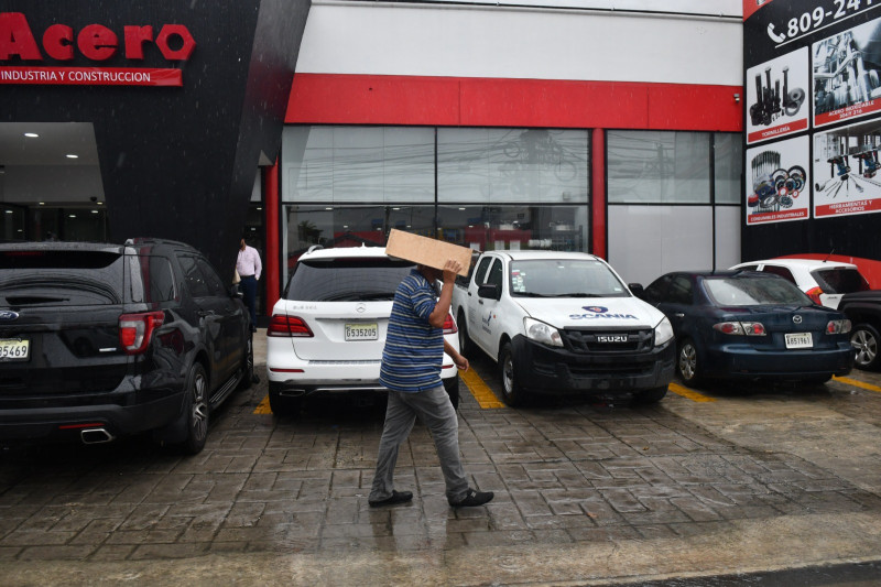 Un hombre se cubre de la lluvia con un pedazo de cartón al caminar por una acera de la capital.