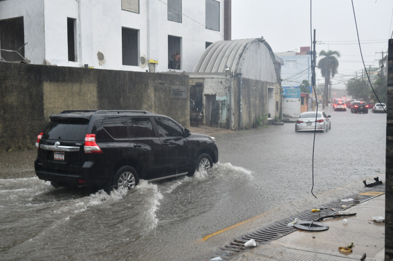 Varios vehículos se desplazan por una calle inundada del Distrito Nacional.