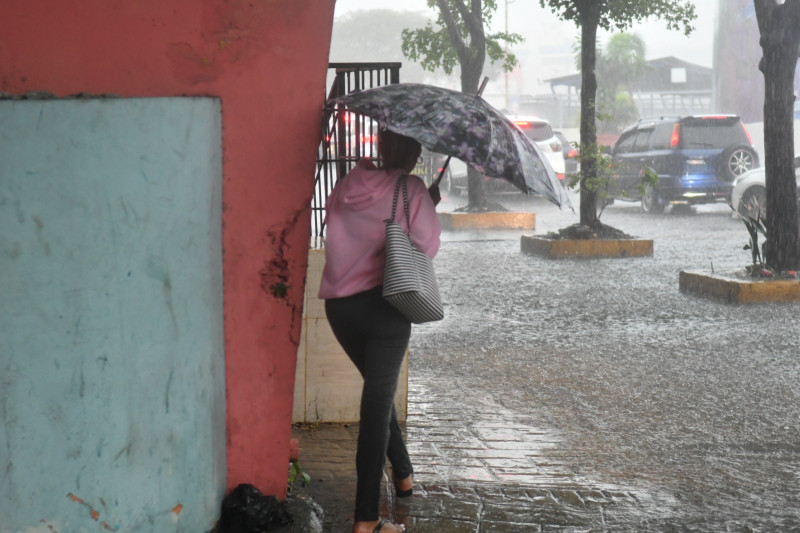 Una mujer se cubre de la lluvia mientras camina por una acera inundada de la capital.