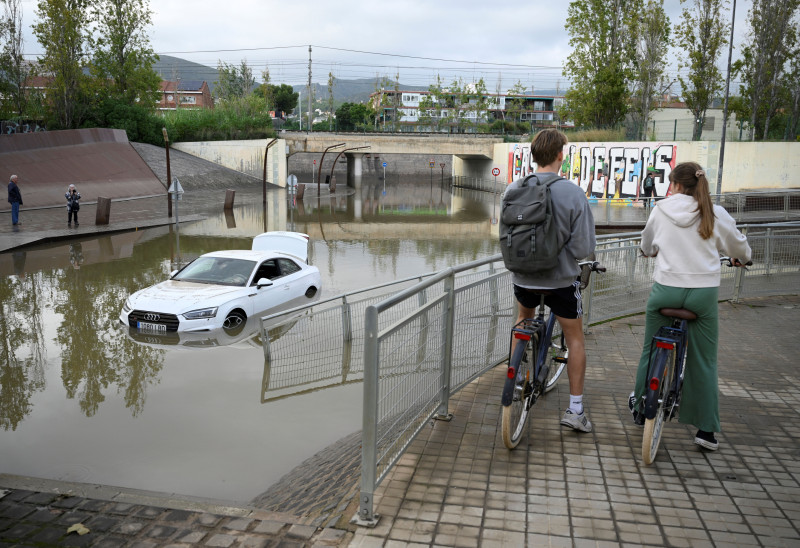 Ciclistas observan un coche inundado en Castelldefels,