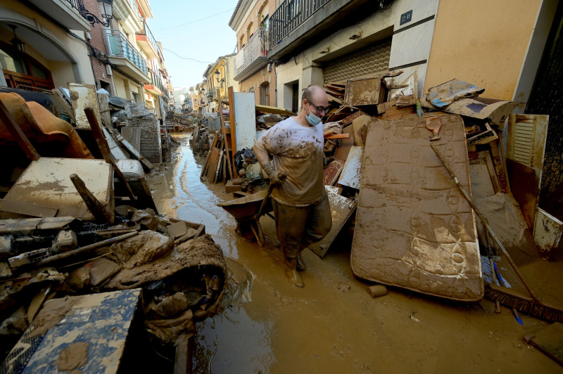 A man with a mask drags a wheelbarrow among mud and debris in a street of Paiporta, south of Valencia, eastern Spain, on November 6, 2024, in the aftermath of deadly floods. - Spain announced an aid package worth 10.6 billion euros ($11.5 billion) to rebuild regions devastated by its worst floods in a generation that have killed 219 people. (Photo by JOSE JORDAN / AFP)