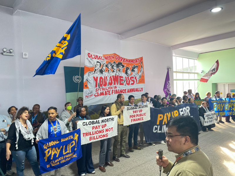 Activistas con pancartas y banderas celebran una reunión para exigir que los países ricos ayuden a las naciones en desarrollo a abordar el calentamiento global.