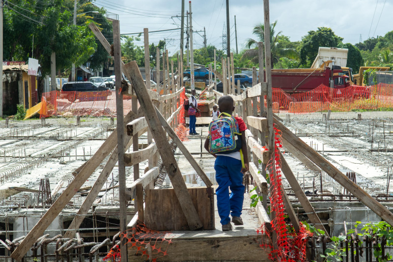 Escolares caminan sobre una columna de concreto de un puente en construcción en Los Alcarrizos, cuyos trabajos están paralizados