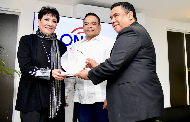 José Ruben Gonell Cosme y Armando Olivero entregan la placa de reconocimiento a Sophy.