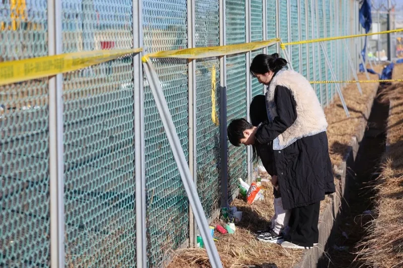 Un niño y su madre hacen una reverencia frente a una valla en el aeropuerto internacional de Muan.