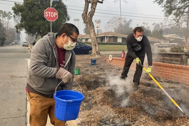 Unas personas vierten agua alrededor de las casas de un vecindario, en Altadena, California (Estados Unidos).