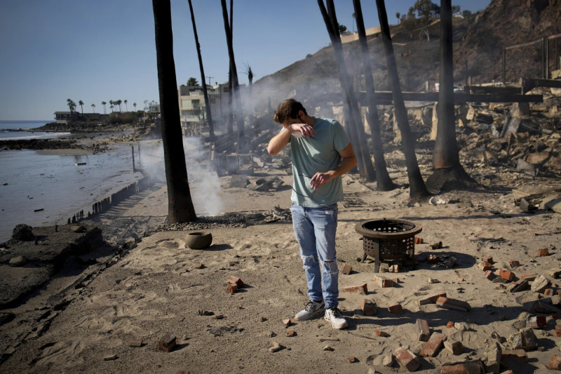 Luke Dexter reacciona mientras examina los restos de la  propiedad frente a la playa de su padre, devastada por el fuego.