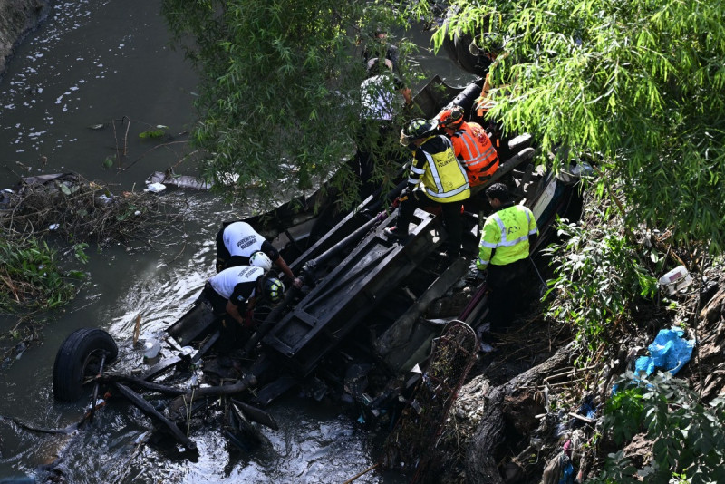 Firefighters work at the scene of an accident in which a bus fell down a ravine in Guatemala City on February 10, 2025. A bus carrying 75 people plunged into a ravine in Guatemala City on Monday, killing at least 31 people, rescue workers said. (Photo by Johan ORDONEZ / AFP)