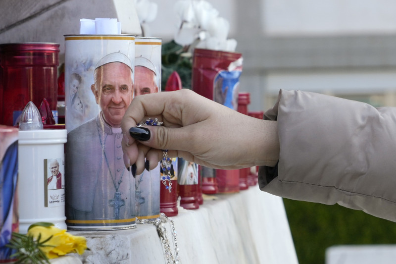 Una mujer deja un rosario junto a velas adornadas con la imagen del papa Francisco, en el exterior del hospital Agostino Gemelli de Roma, donde el pontífice argentino está siendo tratado por una neumonía, en Roma, el 22 de febrero de 2025, (AP Foto/Gregorio Borgia)