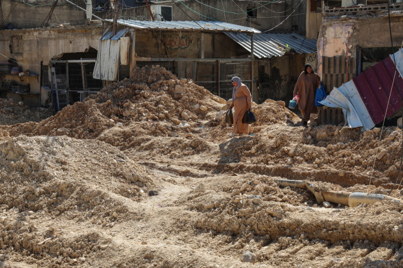 Las personas cargan sus pertenencias mientras cruzan una calle destruida mientras huyen del campo de refugiados palestinos de Nur Shams, cerca de Tulkarem, donde las fuerzas israelíes permitieron a los residentes recuperar sus pertenencias después de emitir notificaciones de demolición de varias casas, en medio de una ofensiva de varias semanas en la Cisjordania ocupada el 26 de febrero de 2025.