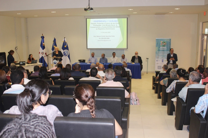 Al fondo, en la mesa principal: Luis Carvajal, de la Comisión Ambiental de la UASD; Francisco Arnemann, del Instituto Dominicano de Desarrollo Integral (IDDI); Jesús Moreno, del Consorcio Ambiental Dominicano (CAD); José Manuel Mateo, de la Academia de Ciencias de República Dominicana;  y Sixto J. Incháustegui, presidente del Grupo Jaragua. En el podio, la bióloga Yvonne Arias, miembro del miembro de la Comisión Mundial de Áreas Protegidas de la Unión Internacional para la Conservación de la Naturaleza (UICN).