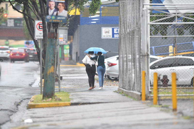 Dos personas caminan bajo la lluvia por una acera de Santo Domingo