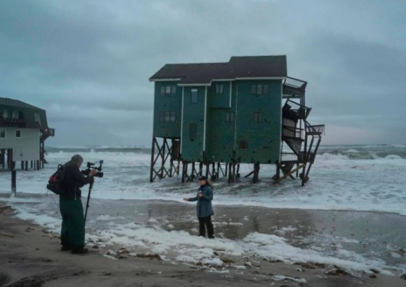 Un reportero de Fox Weather filma frente a una casa en riesgo de derrumbe en medio de una tormenta.