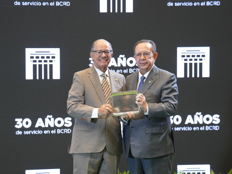 El gobernador del Banco Central, Héctor Valdez Albizu entrega su reconocimiento al escritor José Alcántara Almanzar, Director del Departamento Cultural de la entidad.