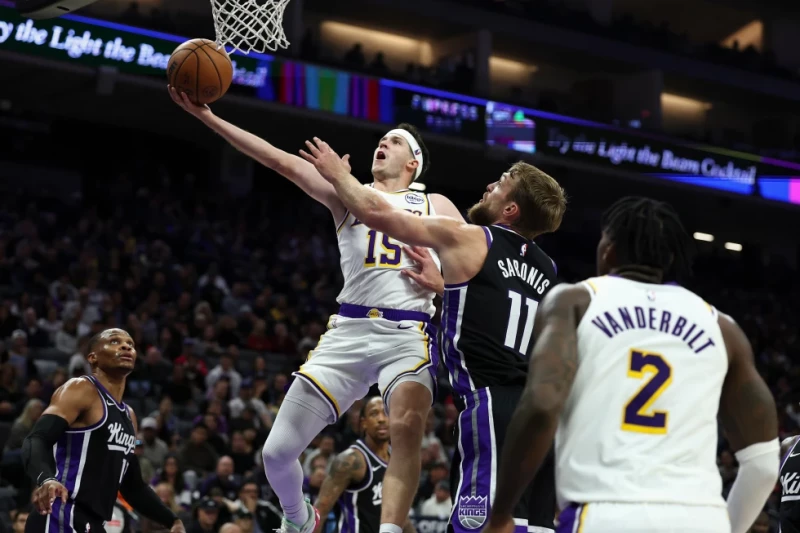 Austin Reaves, izquierda, de los Lakers, recibe una falta de Domantas Sabonis, de los Kings, durante el juego de la NBA, el 26 de octubre de 2025, en Sacramento, California.