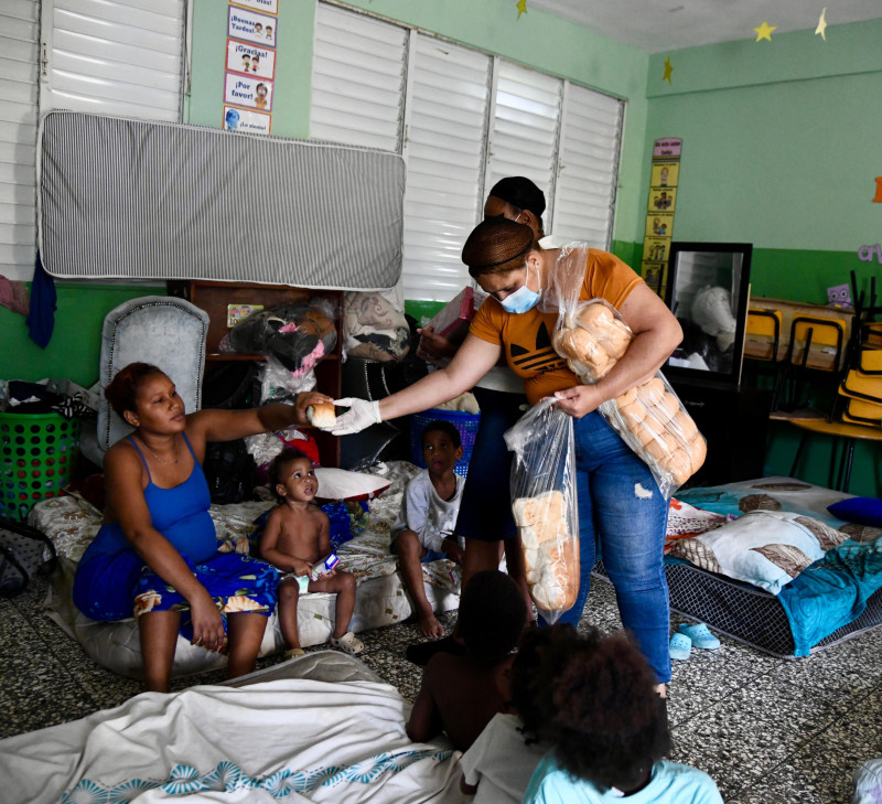 Una madre y sus hijos reciben raciones de pan en el albergue provisional habilitado en la Escuela El Túnel, del sector Capotillo.