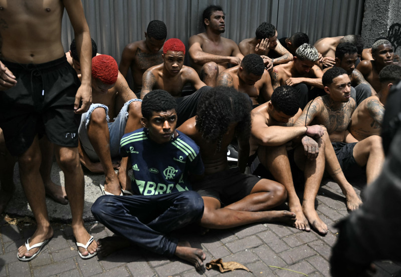Un presunto delincuente arrestado durante la Operação Contenção (Operación Contención) en la favela Vila Cruzeiro mira fijamente a un oficial de policía, en el complejo Penha, en Río de Janeiro, Brasil, el 28 de octubre de 2025.
