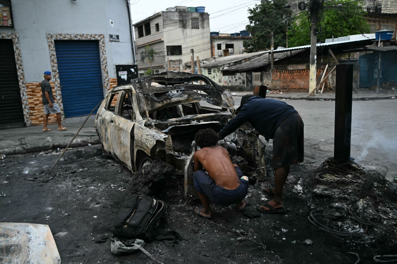 Hombres inspeccionan un automóvil quemado que formaba parte de una barricada instalada durante la Operação Contenção (Operación Contención) en la favela Vila Cruzeiro, en el complejo Penha, en Río de Janeiro, Brasil, el 28 de octubre de 2025.