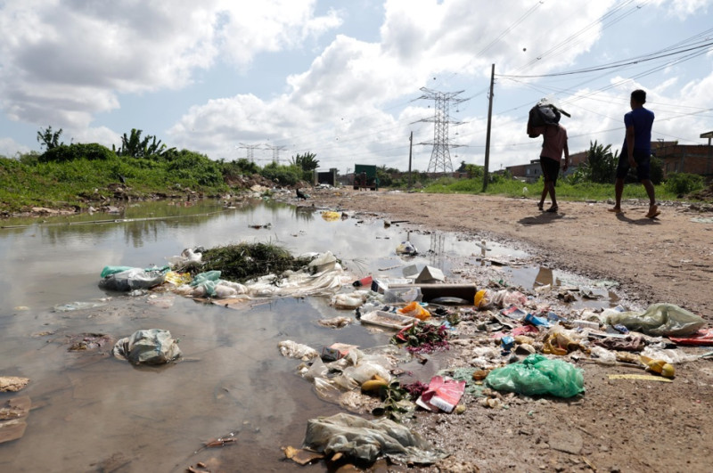 Personas caminan junto a basura en una calle del barrio Maracangalha este viernes, en Belém (Brasil).