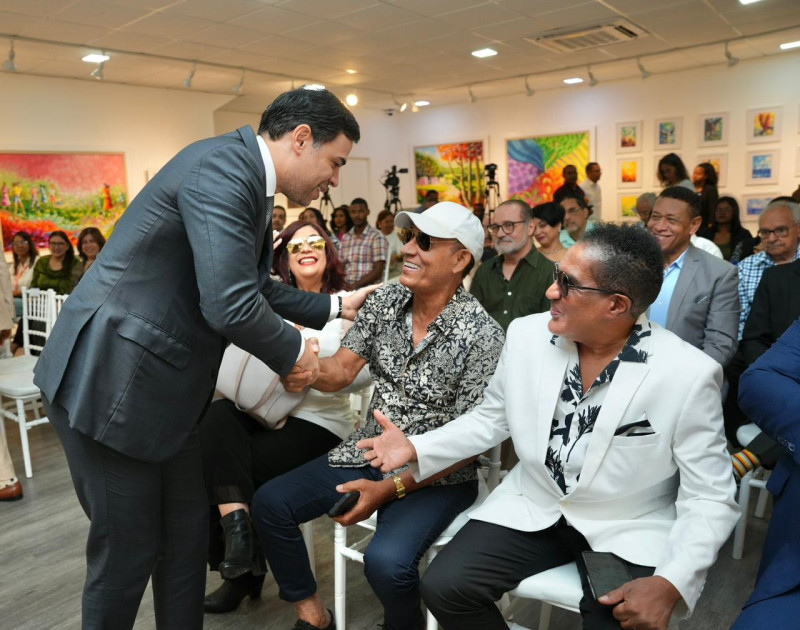 Roberto Ángel Salcedo al saludar a Aníbal Bravo, quien figura sentado junto a Kinito Méndez.