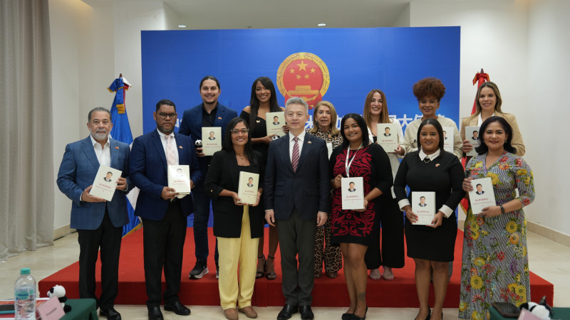 Periodistas dominicanos posan junto al embajador Luning mientras sostienen una obra del presidente chino Xi Jinping sobre la Gobernación y Administración de China.