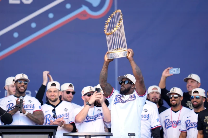 Adolis García, rodeado de sus compañeros de los Rangers, alza el Trofeo del Comisionado durante el festejo por la conquista de la Serie Mundial de 2023.