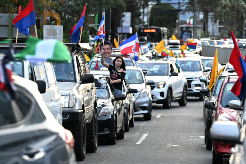 Automovilistas ondeando banderas de diferentes partidos políticos circulan por una calle de San José el 31 de enero de 2026, un día antes de las elecciones presidenciales.