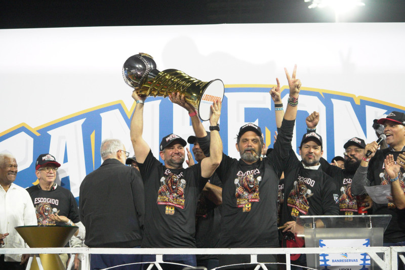 Eduardo Najri y José Miguel Bonetti, principales ejecutivos del Escogido, levantan la copa de campeón del pasado torneo.
