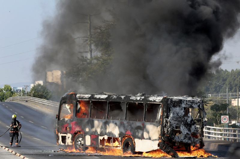 Un bombero extingue un autobús en llamas, incendiado por grupos del crimen organizado en respuesta a un operativo en Jalisco para detener a un objetivo de seguridad de alta prioridad, en una de las principales avenidas de Zapopan, Jalisco, México, el 22 de febrero de 2026.