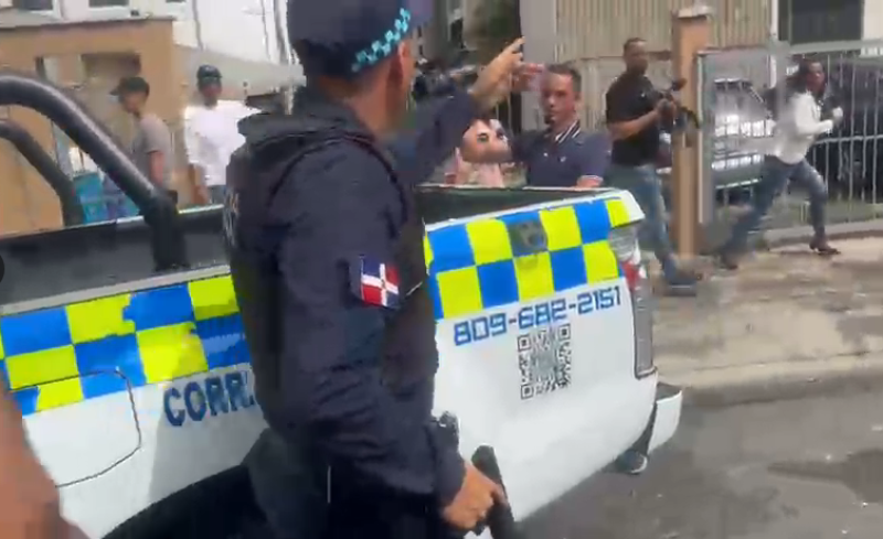 Momento en el que un policía soba su arma de fuego para repeler a miembros de la prensa.