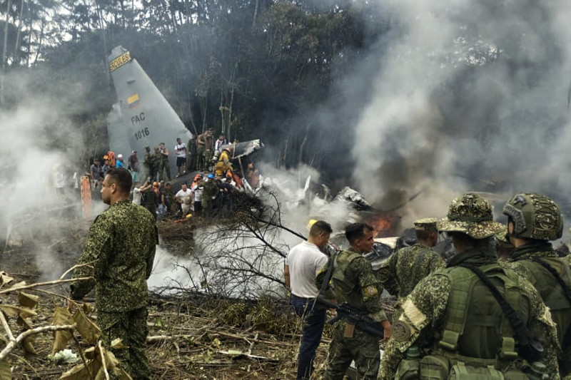 Llamas y una densa columna de humo negro se elevan desde un avión Hércules de la Fuerza Aérea que se estrelló durante el despegue, mientras un miembro de la Policía colombiana permanece cerca, en Puerto Leguizamo, Colombia, cerca de la frontera sur con Ecuador, el 23 de marzo de 2026