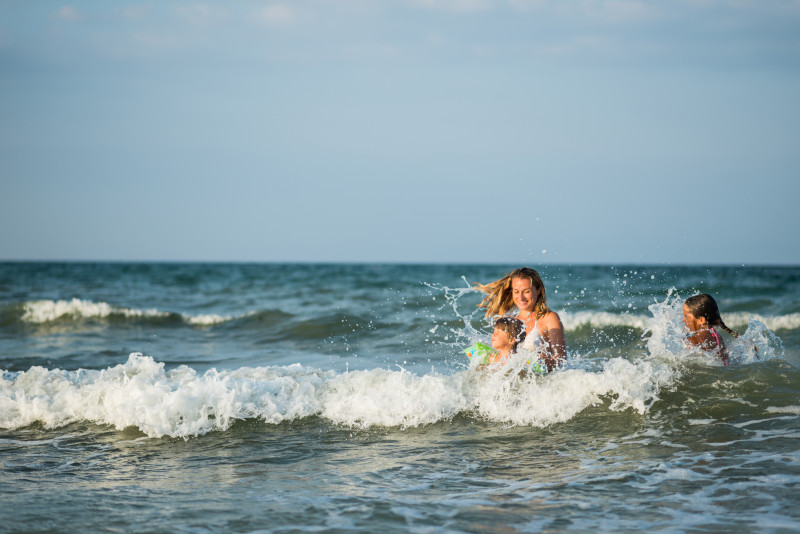 Una madre con sus hijas pequeñas riendo entre las olas del mar en un día soleado.