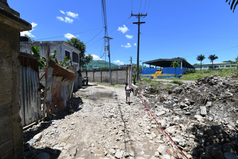 Niños se desplazan a pie cerca de un tramo de pared colapsada en el sector El Portón, en Los Alcarrizos.