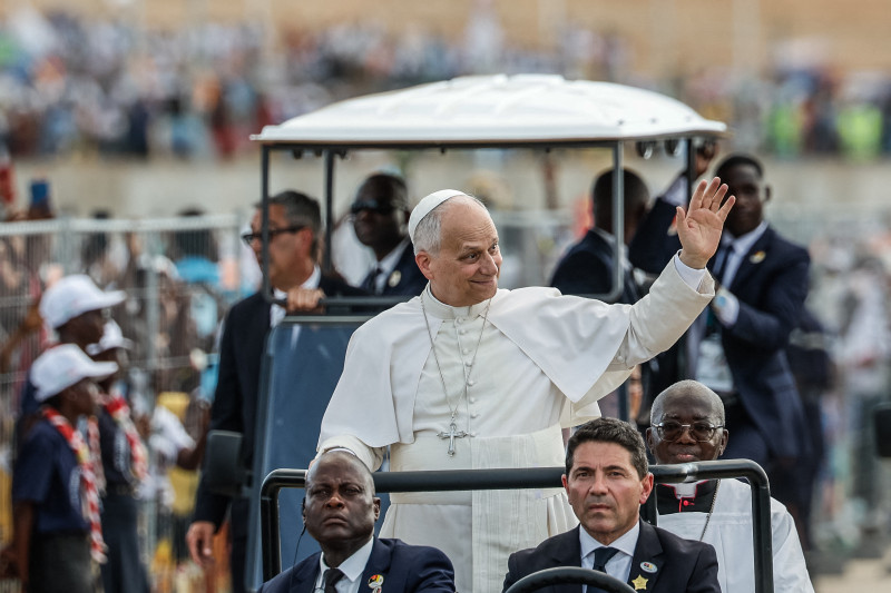 El papa León XIV (C) saluda a la multitud a su llegada para dirigir el rezo del Santo Rosario en la explanada frente al santuario "Mama Muxima" en Muxima