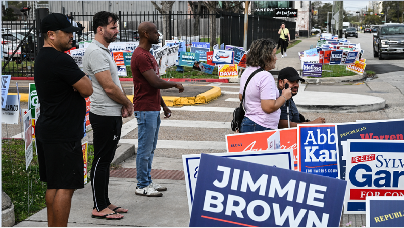 Varias personas pasan junto a carteles de campaña cerca de un centro de votación en el Centro Multiservicios Metropolitano de West Gray, el día de las elecciones en Houston, Texas, el 3 de marzo de 2026.